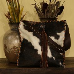 Natural tri-color hair on cow front with brown leather front, sides and back featuring cowhide tassel. Brass D-Rings attach to a removable leather handle with metal accents. Hand laced with saddle tan deer lace and tassel and metal concho accent. This bag is fabric lined and has interior pockets. A classic western handbag to compliment your collection!Handmade in the USA.Custom made to order. Sorry, no returns.Please allow 2-3 weeks for shipping.Dimensions: 17 x 15 Western Leather Bag With Fringe, Western-themed Brown Leather Shoulder Bag, Western Brown Bag With Fringe, Brown Western Bag With Fringe, Luxury Brown Shoulder Bag With Tassels, Western Handbags, Estilo Country, Western Leather, D Rings