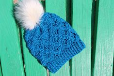 a blue knitted hat with a white pom - pom attached to it