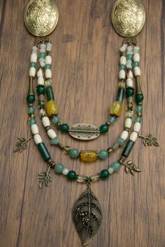 a necklace with beads and charms on a wooden table next to a leaf brooch