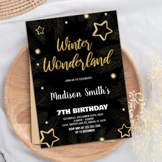 a black and gold winter wonderland birthday party card on top of a wooden platter