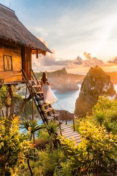 a woman in white dress walking up stairs to a hut on the beach at sunset