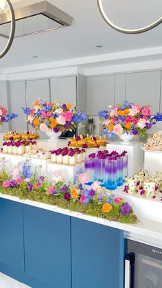 an assortment of cakes and cupcakes on display in a room with blue cabinets