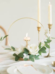 the table is set with white flowers, candles and napkins in gold rimmed holders