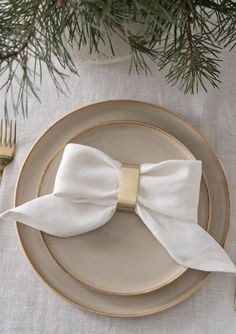 a plate with a white bow on it and gold rimmed place setting for two