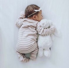 a baby sleeping with a stuffed animal on it's back and wearing a striped outfit