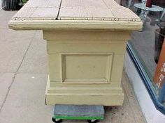 a wooden table sitting on wheels in front of a store window with the door open