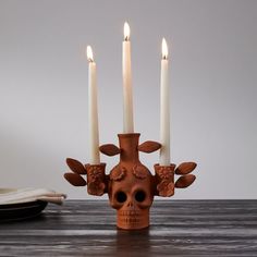 a skull shaped candle holder with three candles in the shape of flowers and leaves on it