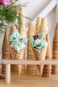 three ice cream cones with green and blue toppings sitting on top of a wooden table