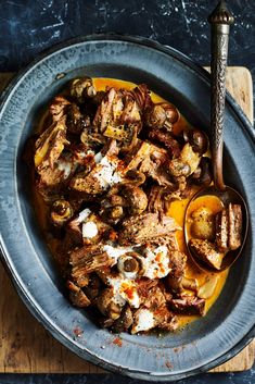 a bowl filled with meat and vegetables on top of a wooden table next to a spoon