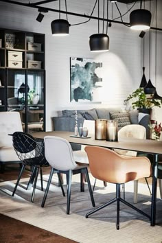 a dining room table with chairs and lights hanging from it's ceiling, in front of a white brick wall