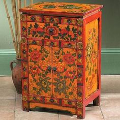 an orange and red painted cabinet with bamboo sticks in it's holder next to a potted plant