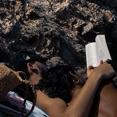 a man reading a book while laying on the ground next to some rocks and mountains