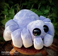 a blue stuffed animal with big eyes sitting on a wooden table in front of some plants