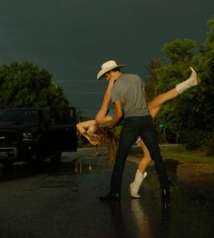 a man and woman dancing in the rain under a dark sky with storm clouds behind them