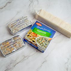 three packages of frozen food sitting on top of a marble counter next to two plastic containers