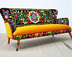 an orange couch with colorful floral designs on it's back and legs, sitting on a wooden floor