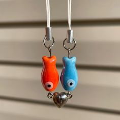 two small ceramic animals hanging from hooks on a wall ornament with a heart in the middle