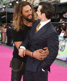 two men in suits are hugging on the pink carpet