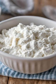 a white bowl filled with cottage cheese on top of a blue and white towel next to a wooden table