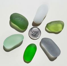 six different colored stones sitting next to a quarter penny on a white surface with space for text