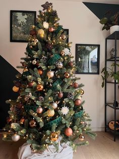 a decorated christmas tree in a living room with pictures on the wall and wooden floors