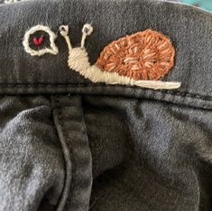 an embroidered snail on the back of a pair of jeans