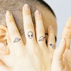 two fingers with small tattoos on them, and an alien face tattoo behind the finger