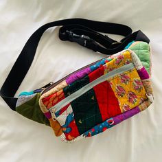 a multicolored patchwork purse sitting on top of a white sheet covered bed