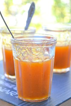 two glasses filled with orange juice on top of a blue table cloth next to a spoon