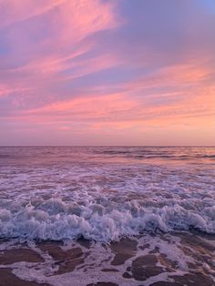 the sky is pink and purple over the water at sunset on the beach with waves coming in