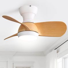 a white ceiling fan with wooden blades in a living room or dining room area next to a window