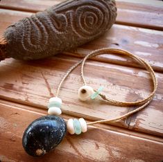 two necklaces are sitting on a wooden table next to a rock and an object