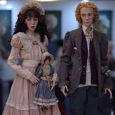 two dolls dressed in period clothing standing next to each other