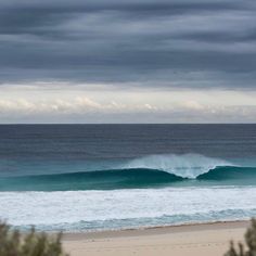 an ocean view with waves crashing on the beach and dark clouds in the sky above