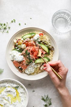 a person holding chopsticks over a bowl of food with cucumbers and tomatoes