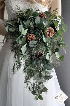 a bride holding a bouquet of greenery and pine cones