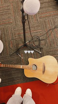 an acoustic guitar sits on the floor in front of a microphone and other musical equipment