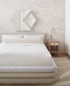 a white bed sitting in front of a brick wall next to a nightstand with a mirror on top of it