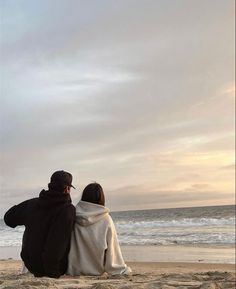 two people sitting on the beach looking out at the ocean