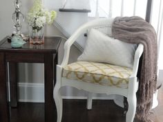 a white chair sitting next to a small table with flowers on it and a blanket draped over it