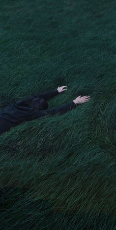 a man laying in the grass with his hands out to catch something while wearing a black suit