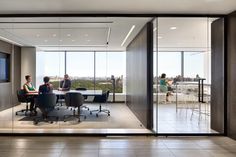 two people sitting at a table in an office with large glass walls and floor to ceiling windows