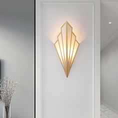 a wall light that is on the side of a white door next to a vase with flowers in it