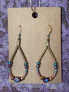 Gold and Imperial Jasper Dangle Earrings. The colors are purple, pink, turquoise, blue, and gold. The center stone is Imperial Jasper, gold, turquoise, pink and purple seed beads line each side of the Jasper. Perfect earrings for dressing up or wearing just your blue jeans and a t-shirt. Purple Teardrop Earrings With Dangling Beads, Purple Gemstone Earrings With Round Beads, Purple And Gold Beaded Earrings, Purple Earrings With Dangling Round Beads, Purple Metal Beaded Drop Earrings, Turquoise Roses, Imperial Jasper, Pink Turquoise, Seed Bead Earrings