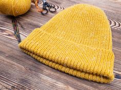 a yellow knitted beanie sitting on top of a wooden floor next to scissors