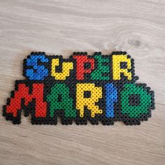 the word super mario spelled with beads on top of a wooden table next to a pair of scissors