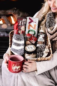 a woman is holding a basket with coffee and snacks in it while sitting next to a fireplace