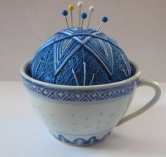 a blue ball of yarn sitting in a white cup with needles sticking out of it