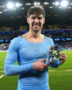 a man holding a soccer ball and trophy in front of a stadium filled with people