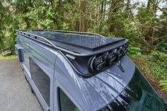 a van with solar panels on the roof is parked in front of some pine trees